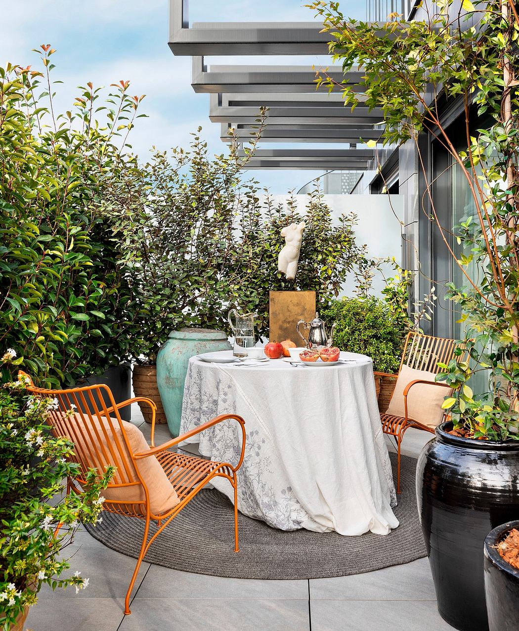 An outdoor dining area with a modern, minimalist aesthetic featuring a table set for a meal, surrounded by lush greenery and stylish furniture.