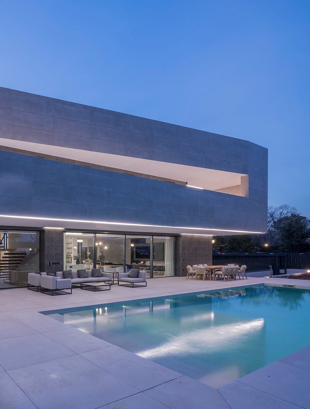 A modern two-story building with sleek angular design, surrounded by a pool and outdoor seating.