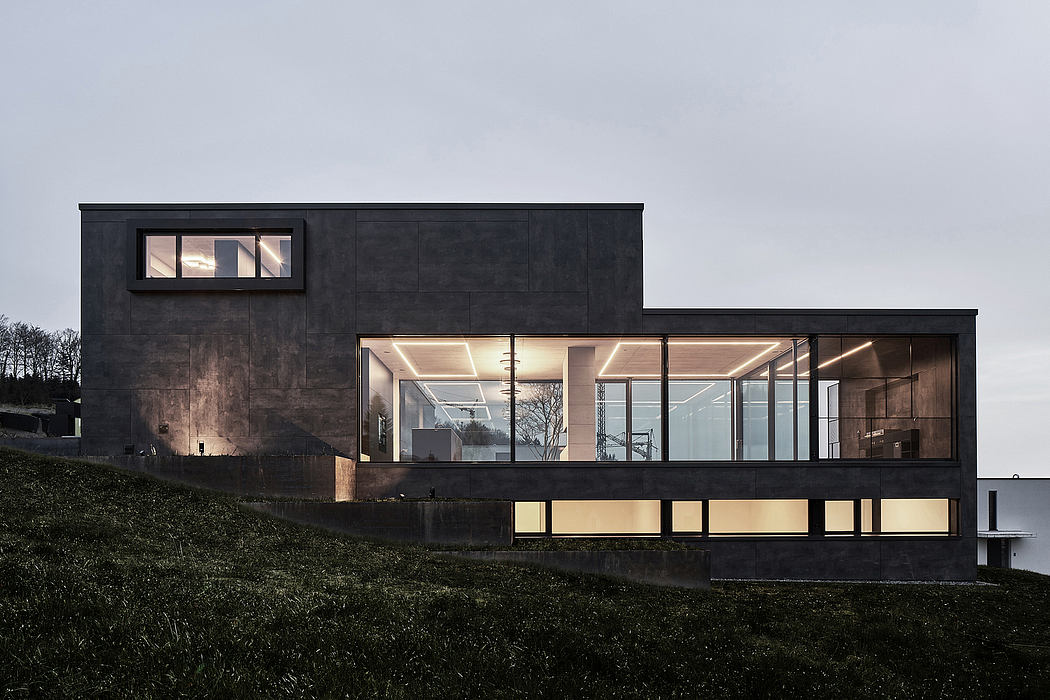 A sleek, modern building with large glass windows and a dark exterior, nestled in a grassy hillside.