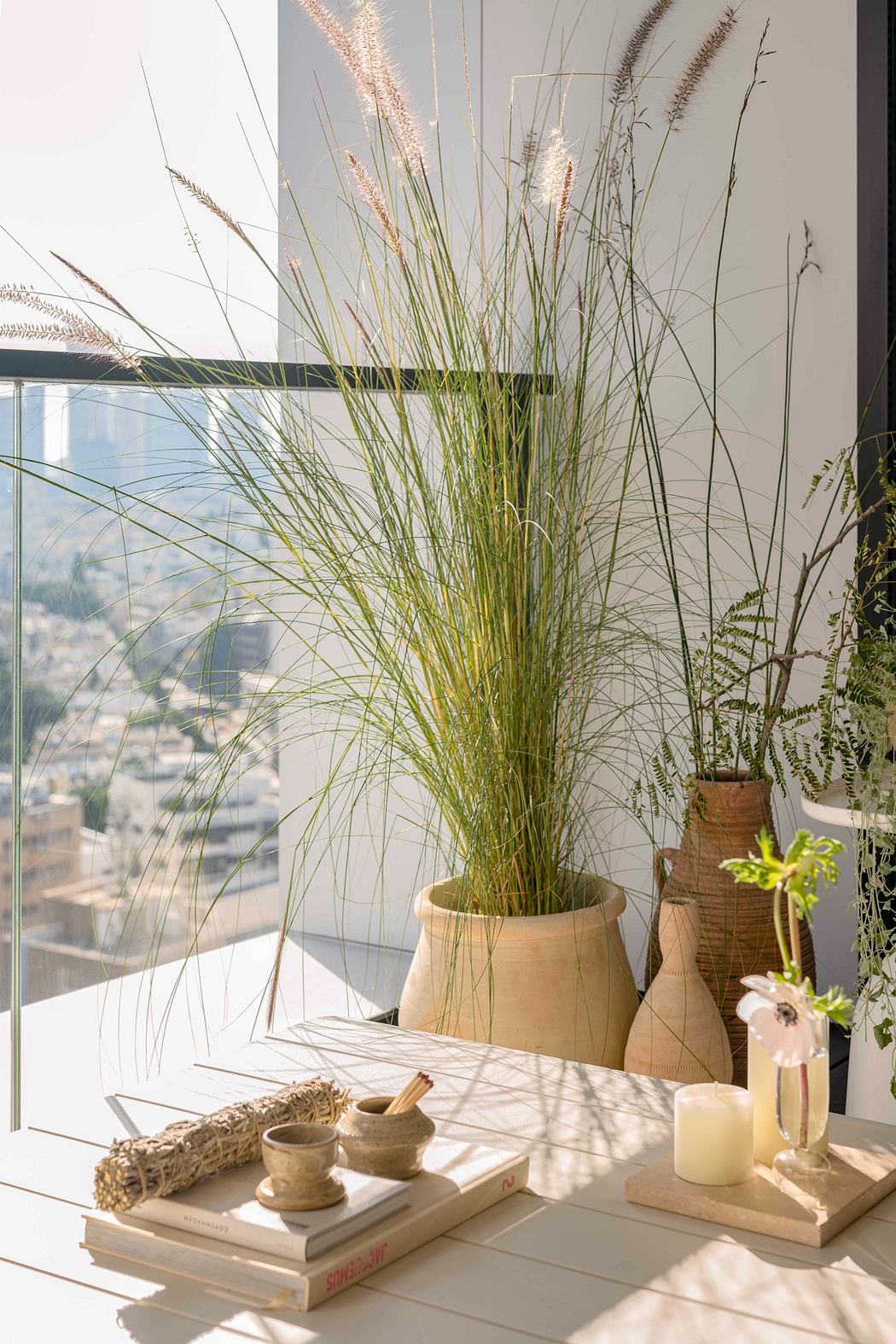 A cozy interior with a tall potted plant, ceramic vases, and books on a minimalist table.