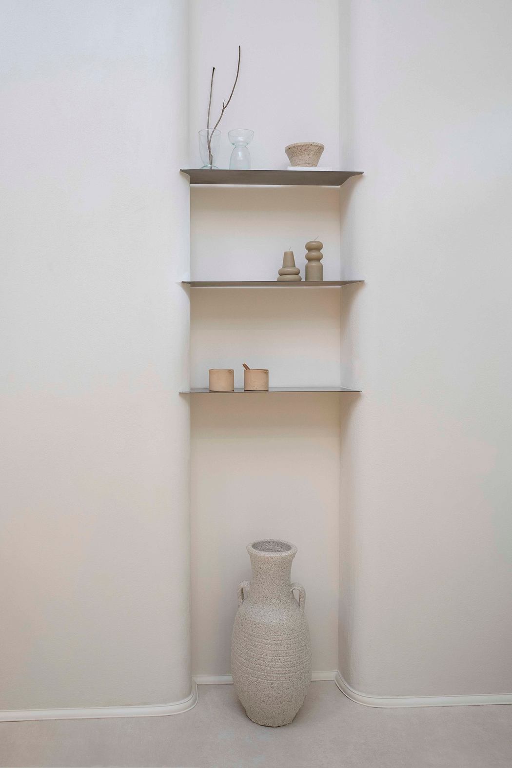 Minimalist shelving unit with various decorative objects and vase in a neutral-toned interior.