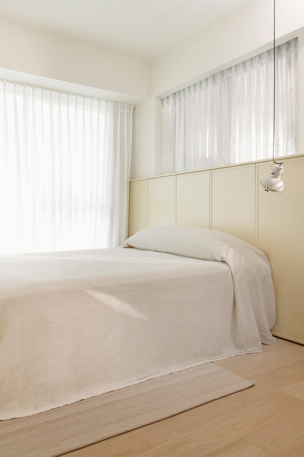 A minimalist bedroom with clean lines, beige tones, and a floor-to-ceiling window providing ample natural light.