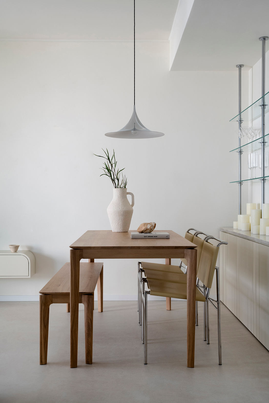 A minimalist dining area with a wooden table, chairs, and a pendant light fixture. The room features clean lines and a calming, neutral palette.