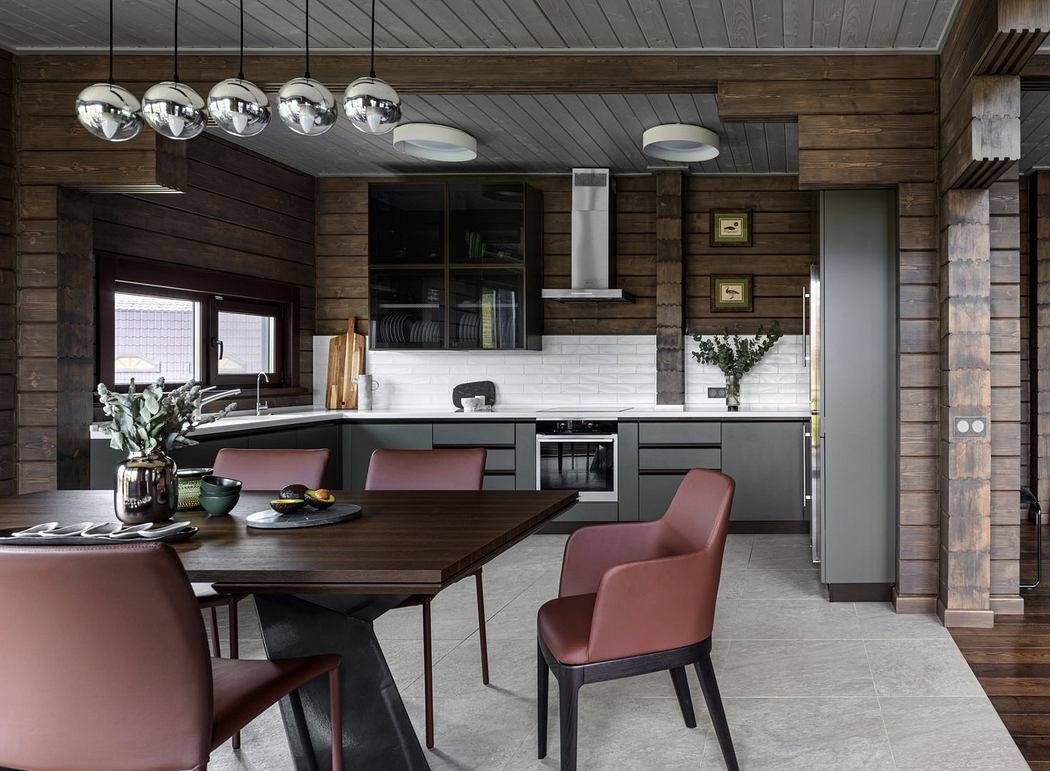 Rustic cabin kitchen and dining area with wooden walls, modern lighting, and burgundy chairs.