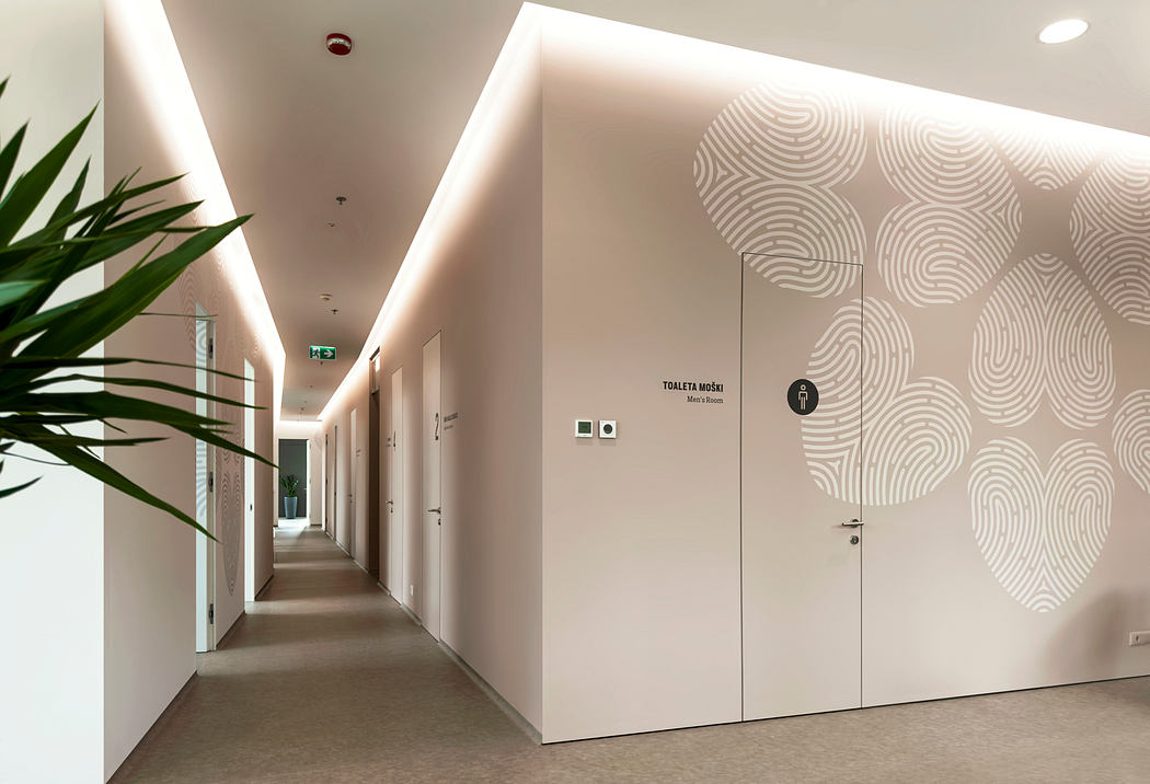 A modern, well-lit corridor featuring patterned walls, recessed lighting, and potted plants.