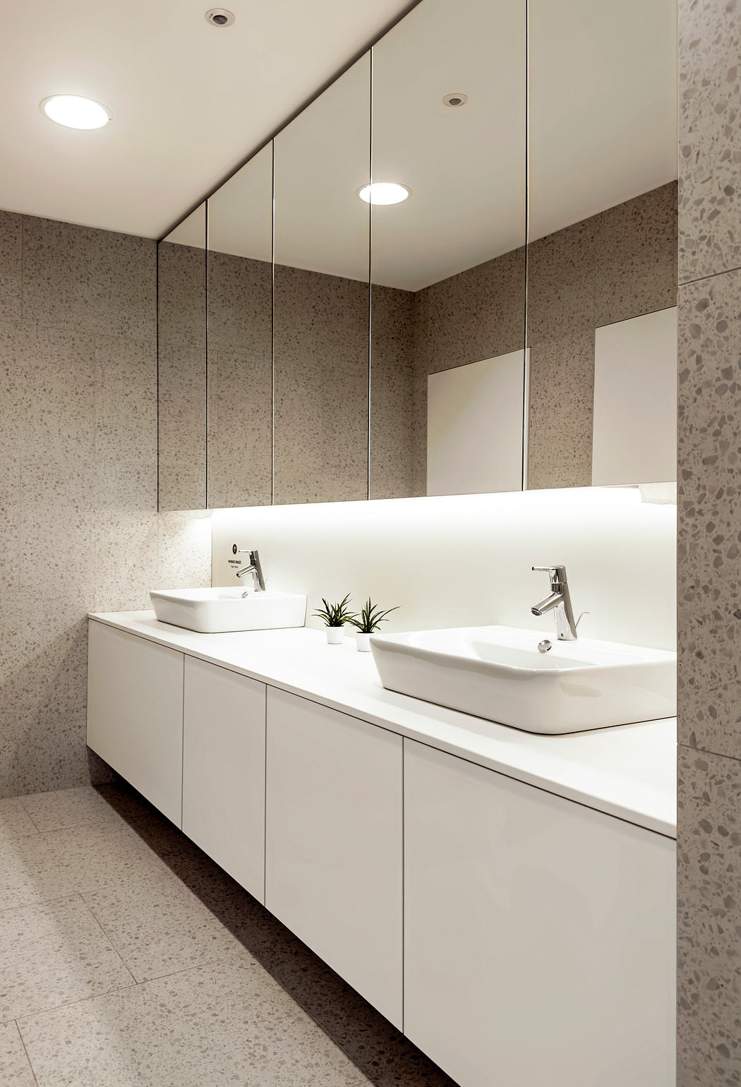 Sleek, modern bathroom with dual vessel sinks, recessed lighting, and terrazzo walls.