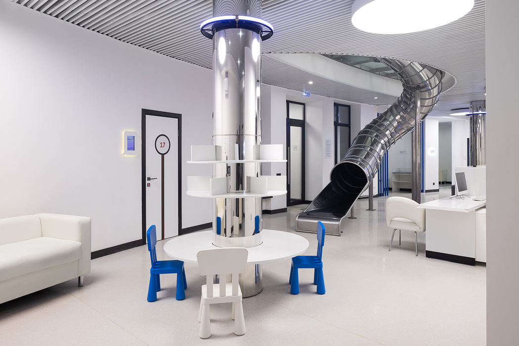 Modern, futuristic interior with white furniture, spiral slide, and cylindrical lighting fixture.