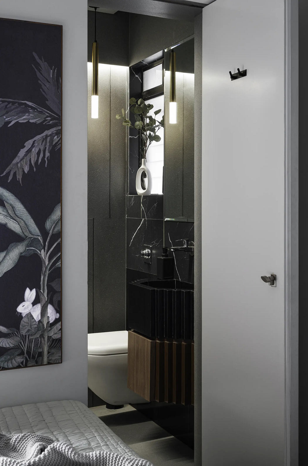 A sleek, modern bathroom with black marble tiles, brass fixtures, and a stylish floral arrangement.