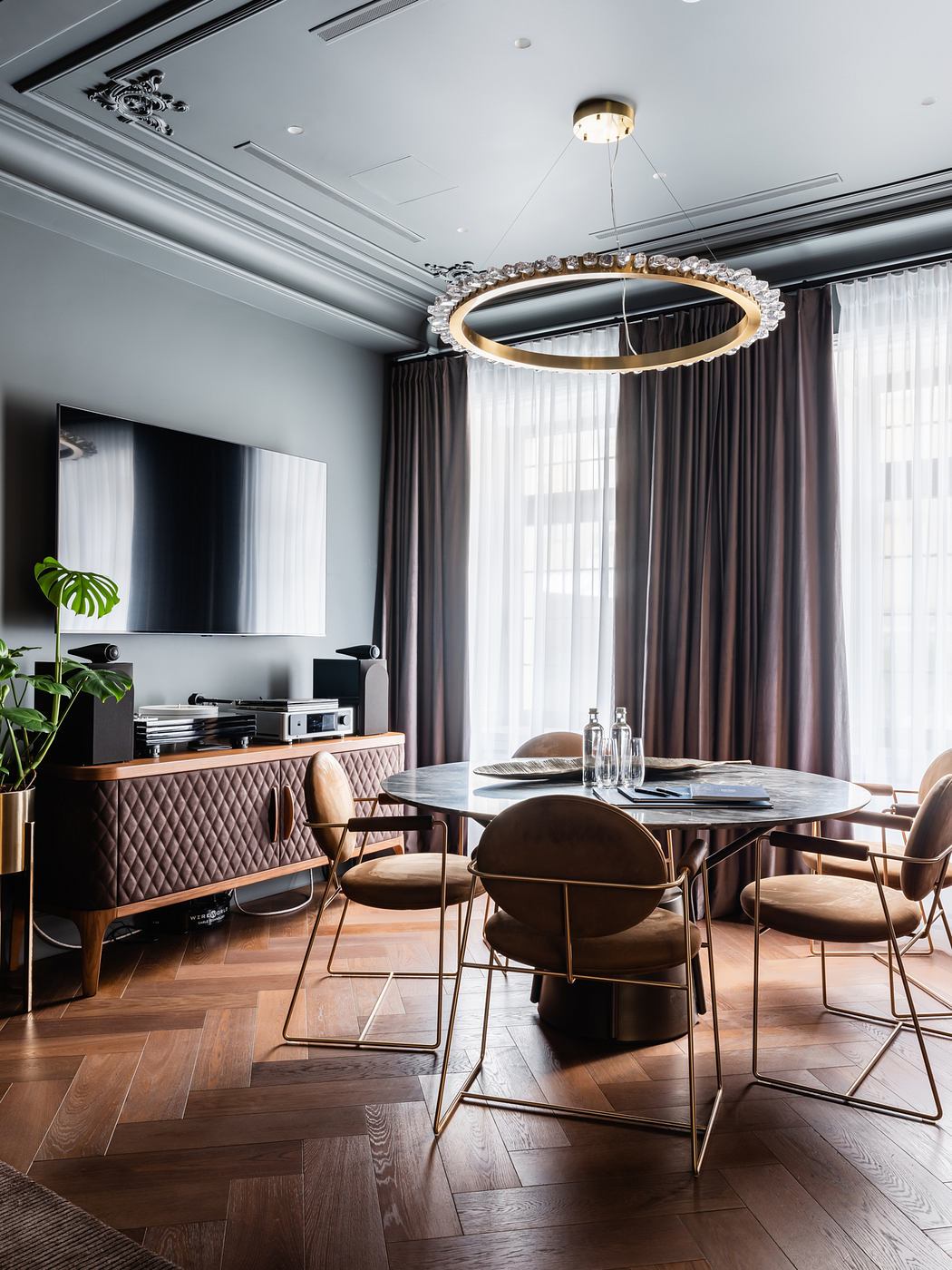 Elegant dining room with circular chandelier, plush chairs, and wooden credenza.
