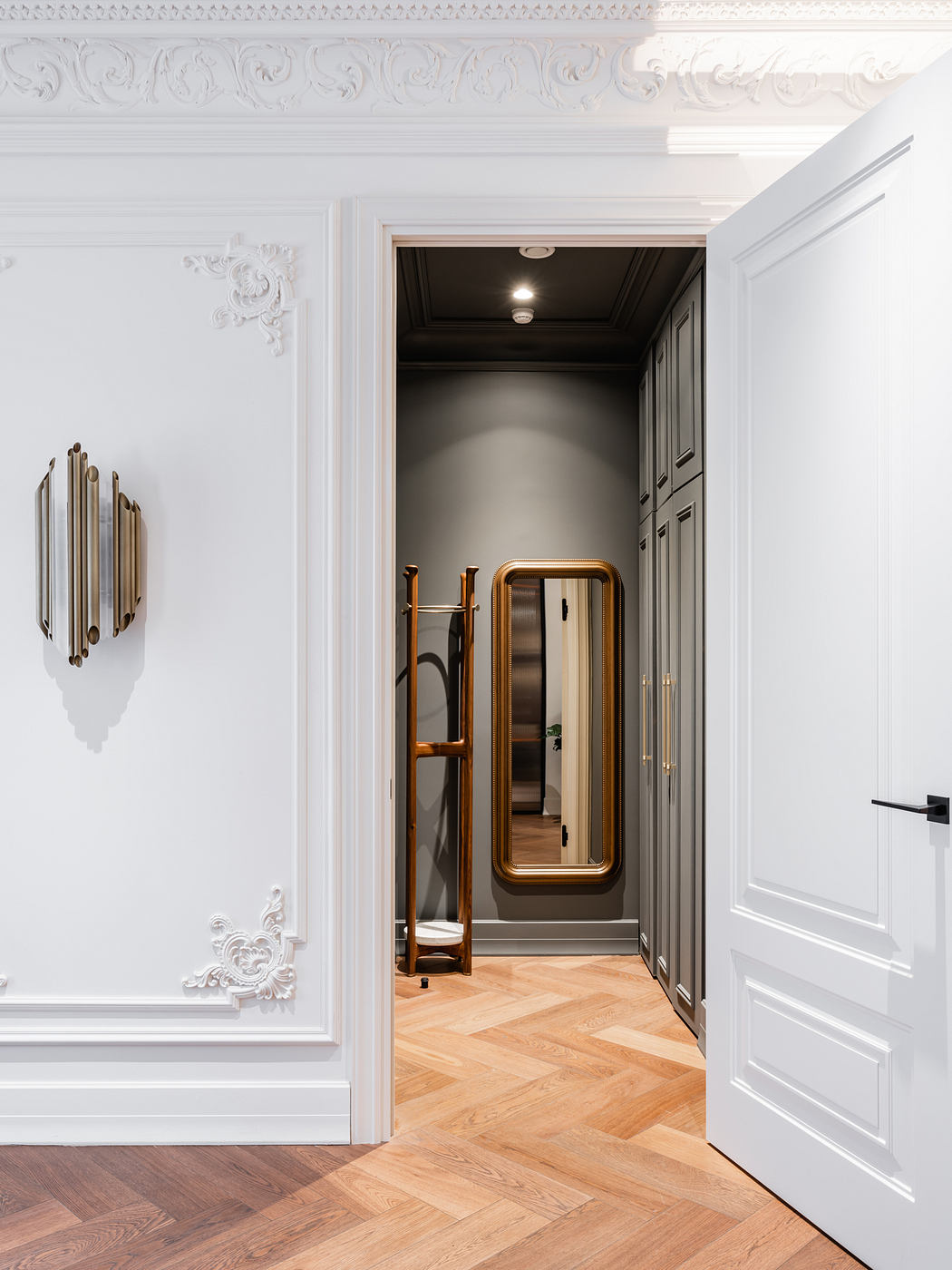 Ornate molding, herringbone floors, and a grand mirror frame the entryway.