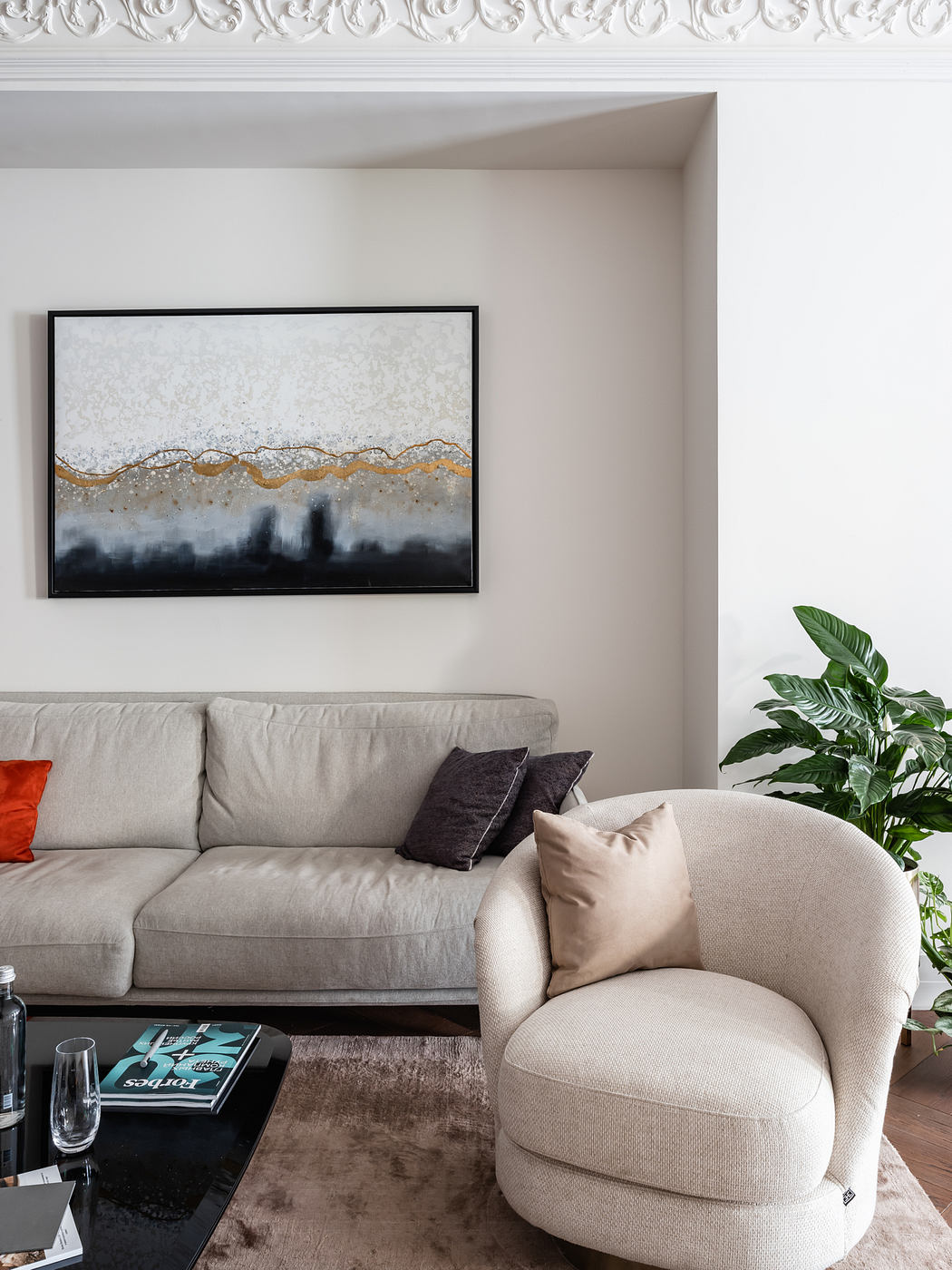 Elegant living room with abstract painting, plush furniture, and lush greenery.