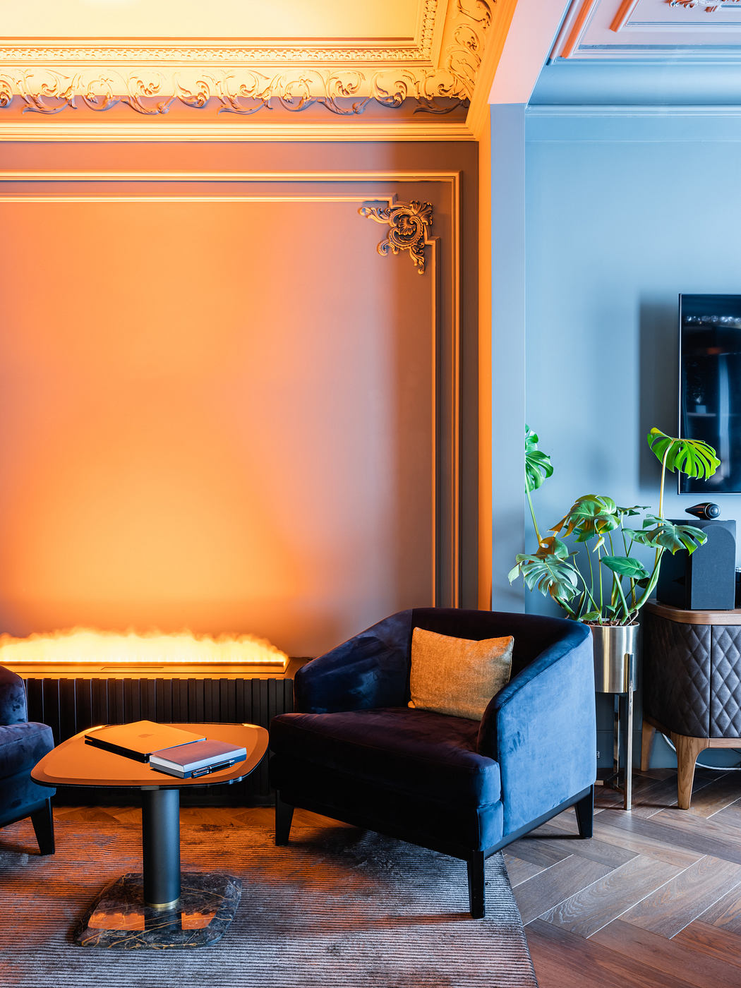 Ornate gold framing, plush blue sofa, and potted plant accent a cozy living space.