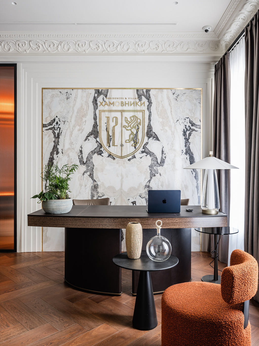 Marble-clad wall with ornate molding, dark wood desk, and plush orange chair in modern office.