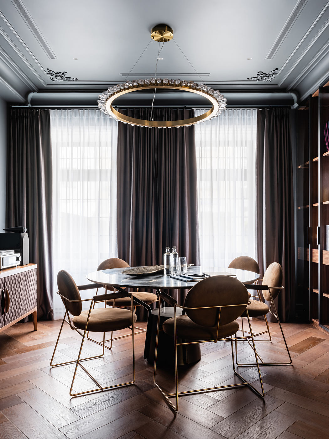 Luxurious dining room with a sleek, circular chandelier, dark curtains, and sophisticated furnishings.