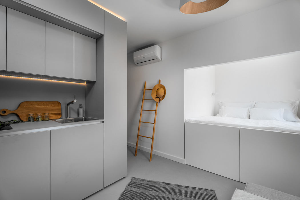 Modern, minimalist studio apartment with sleek gray cabinets, wooden accents, and a ladder decoration.