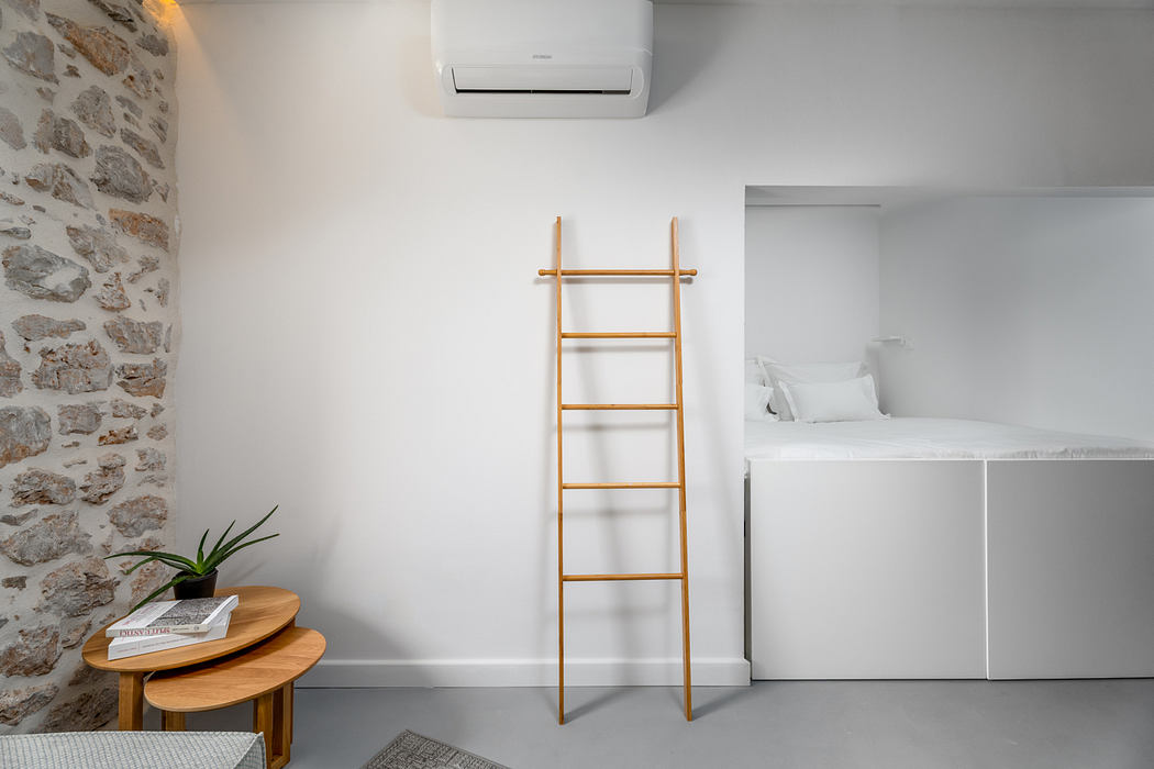 Modern studio apartment with wooden ladder, stone wall, and minimalist decor.