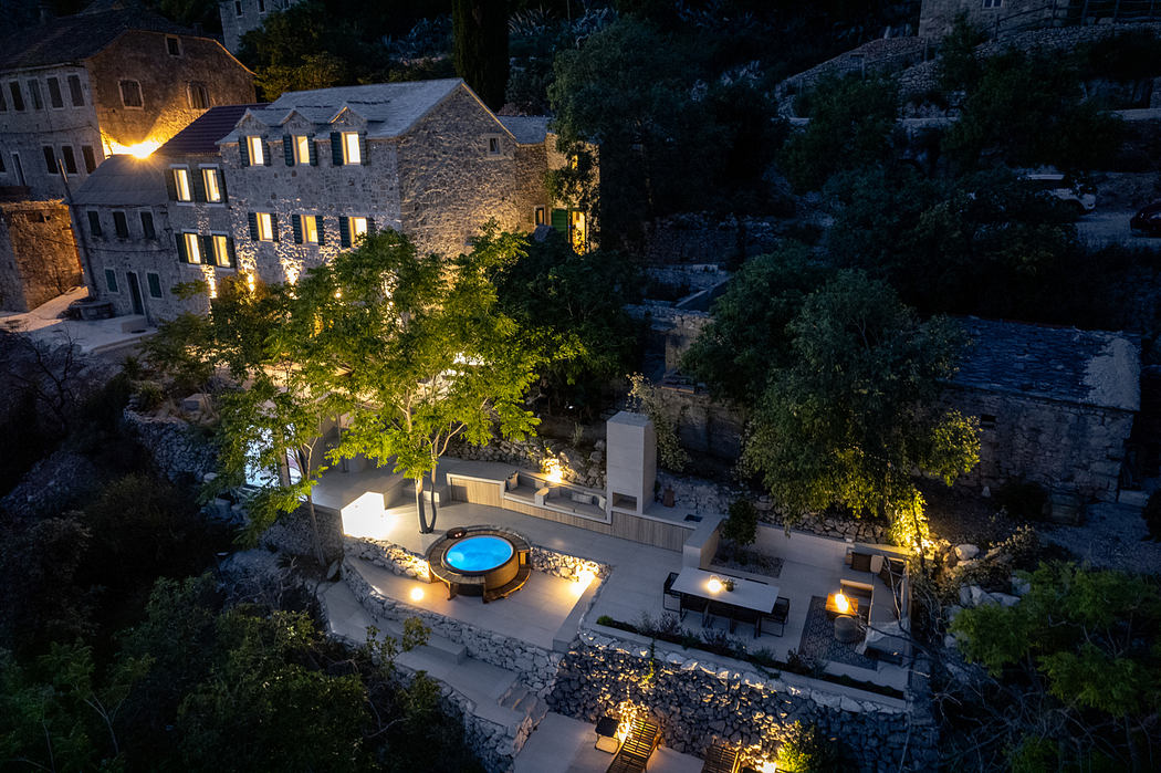 Idyllic stone-walled complex with illuminated pool and patio against a forest backdrop.