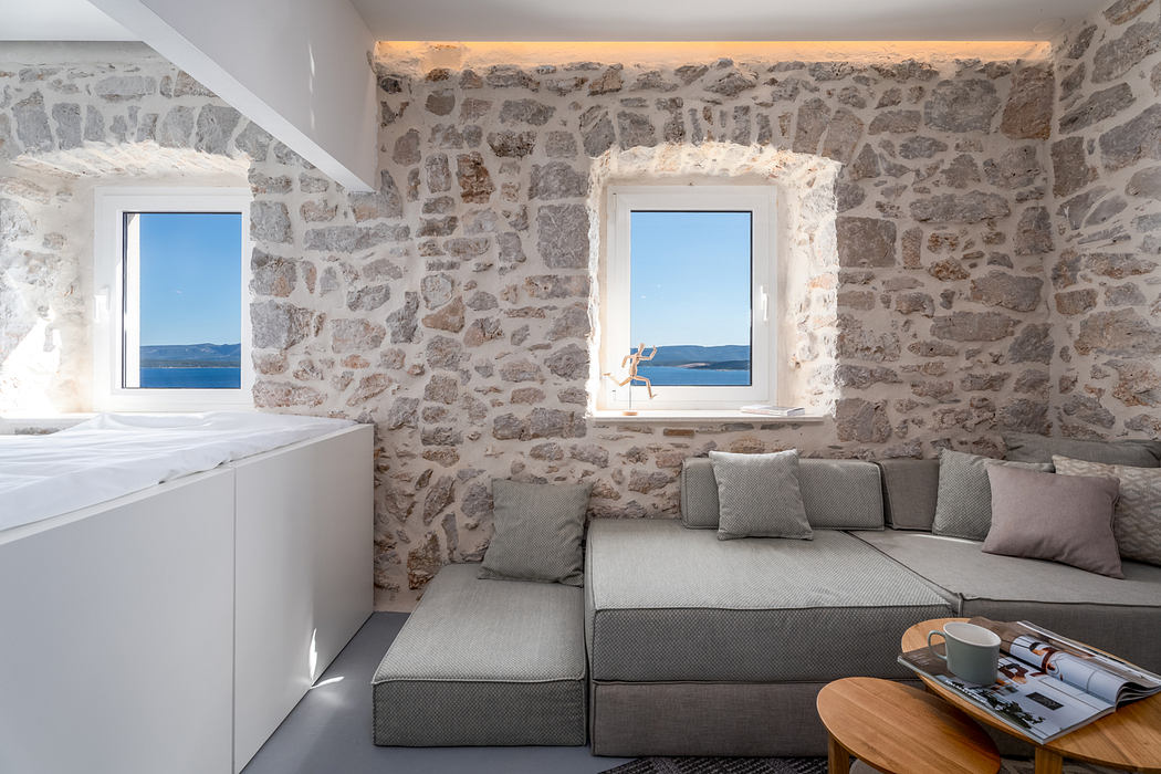 Cozy stone-walled room with large windows offering stunning sea views, minimalist furnishings.