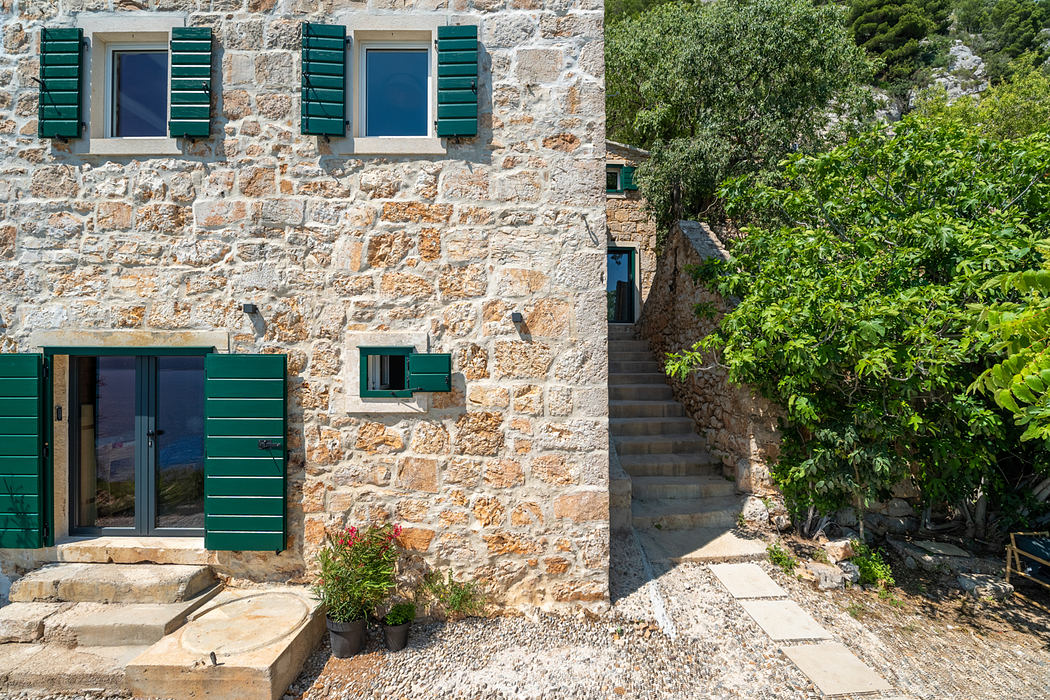 Rustic stone building with green shutters and a winding staircase leading up.