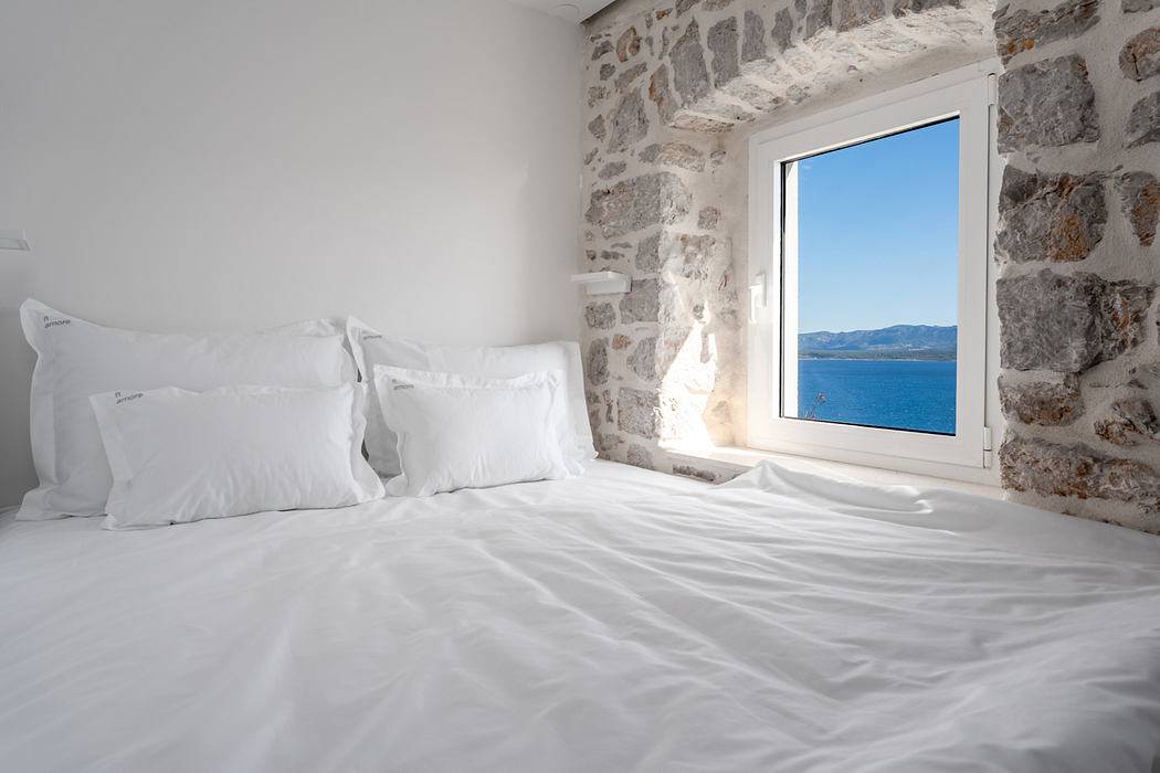 Cozy stone-walled bedroom with panoramic ocean view through large window.