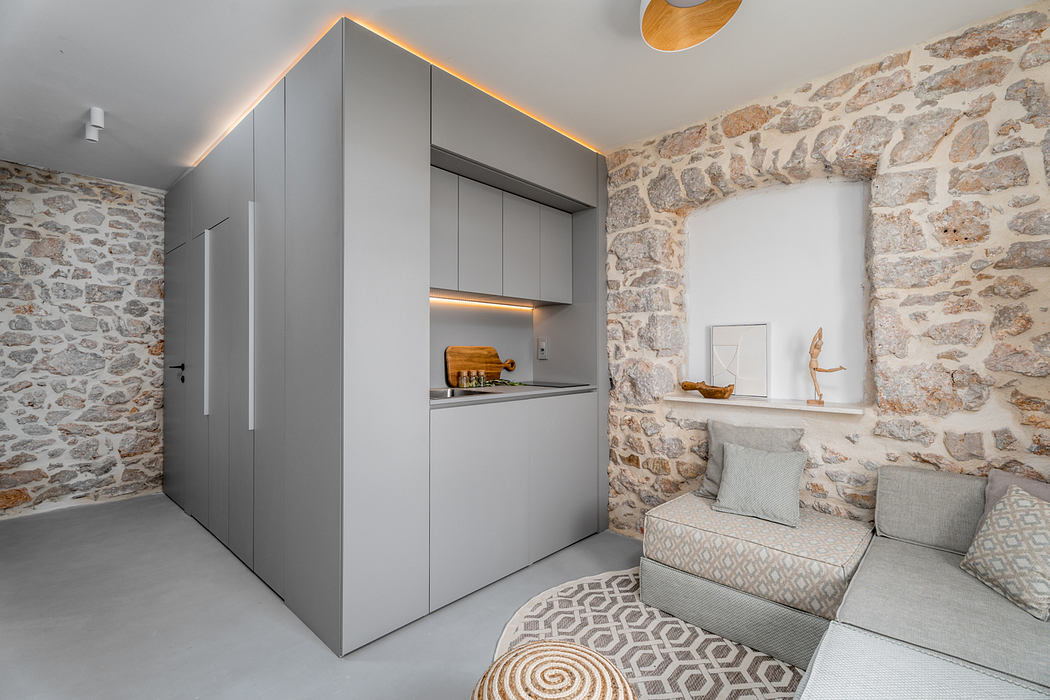 Minimalist kitchenette in a stone-walled room, with a cozy seating area and decor.