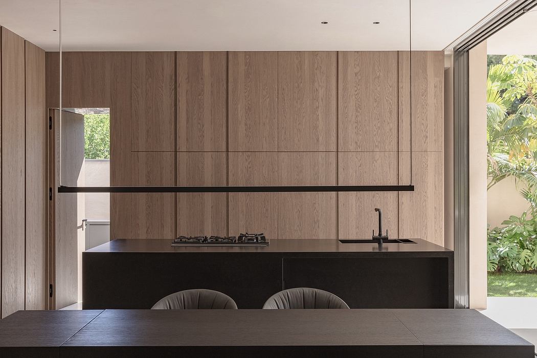 A modern kitchen with dark wood paneling, a sleek black counter, and a minimalist design.