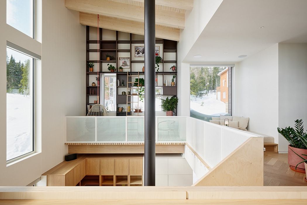 Modern open-concept interior with wooden accents, built-in shelving, and large windows overlooking a snowy landscape.