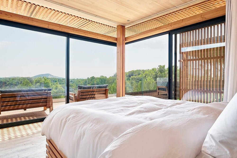 Expansive glass walls, warm wood beams, and serene nature views define this modern bedroom.