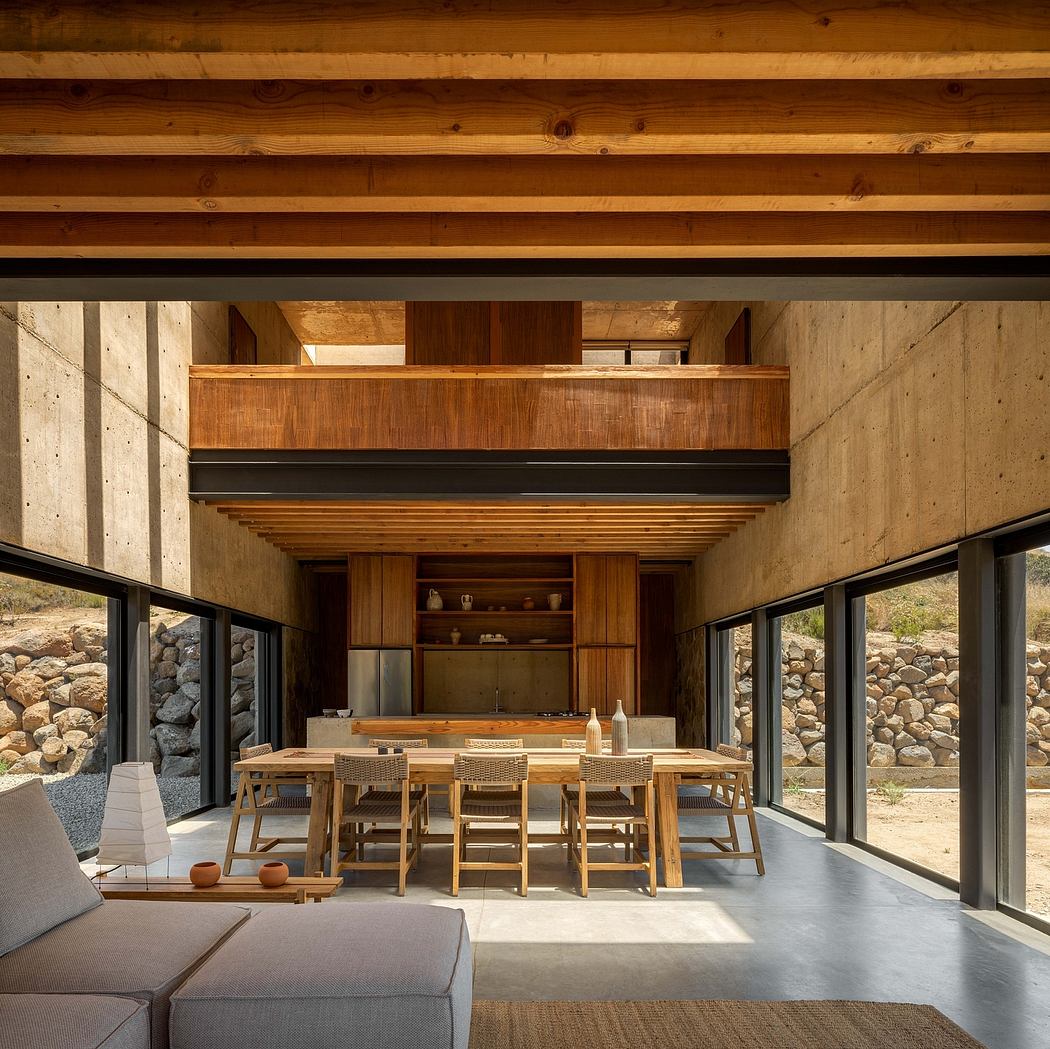 A rustic, open-plan kitchen and dining space with wood-paneled walls, large windows, and a concrete floor.