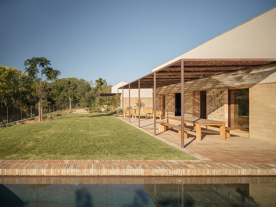 A modern, single-story building with a covered porch, surrounded by lush greenery and a reflection pool.