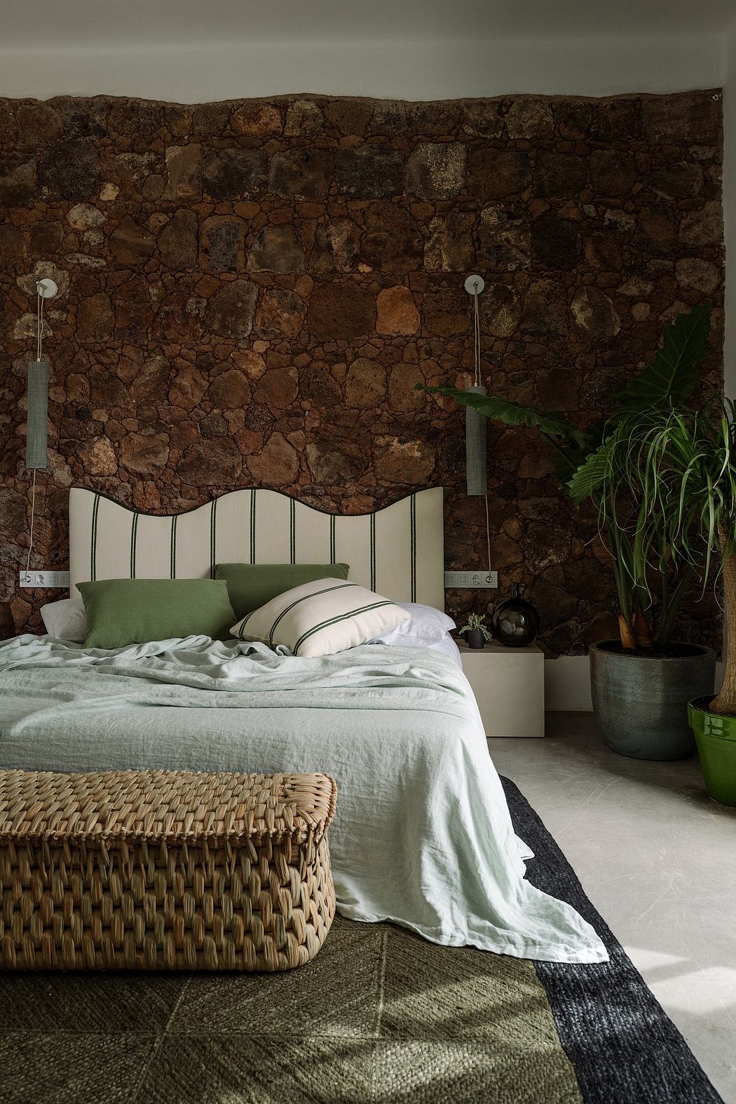 Rustic stone wall, woven rattan bed frame, lush greenery, minimal decor in earthy tones.