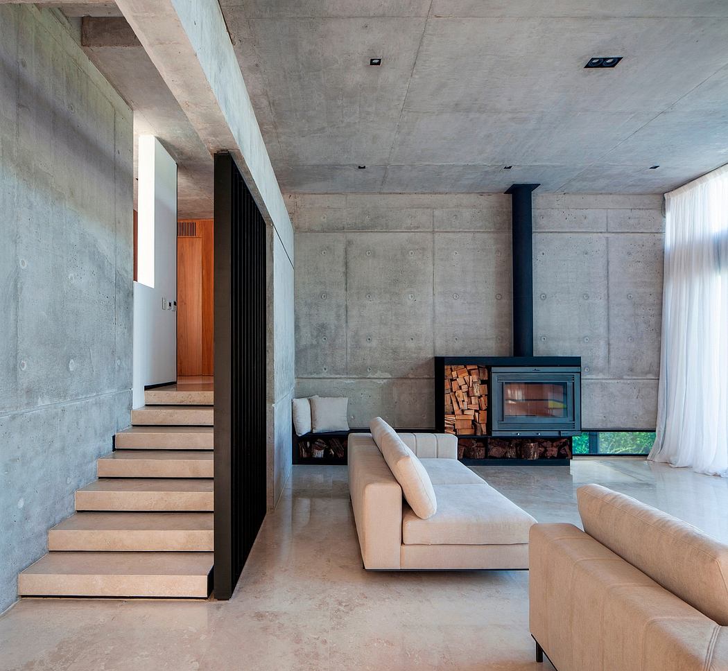 Minimalist concrete interior with wood-burning stove, cozy lounge seating, and open staircase.
