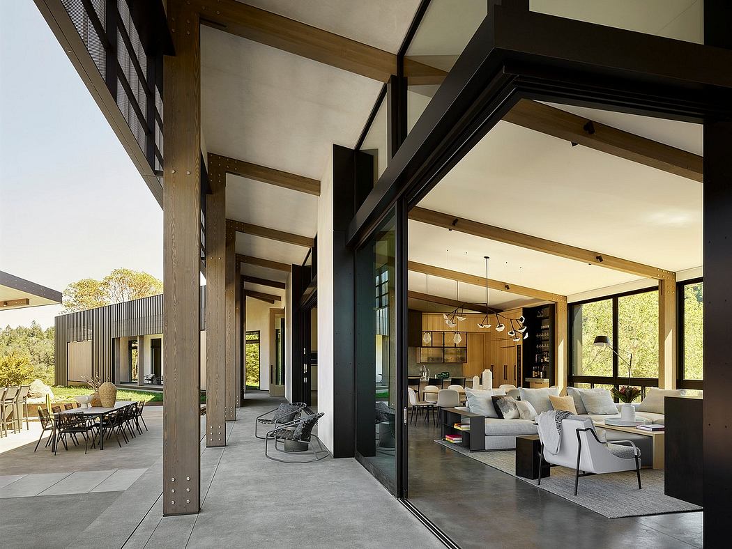 Contemporary open-plan living area with exposed wood beams, large windows, and outdoor dining.
