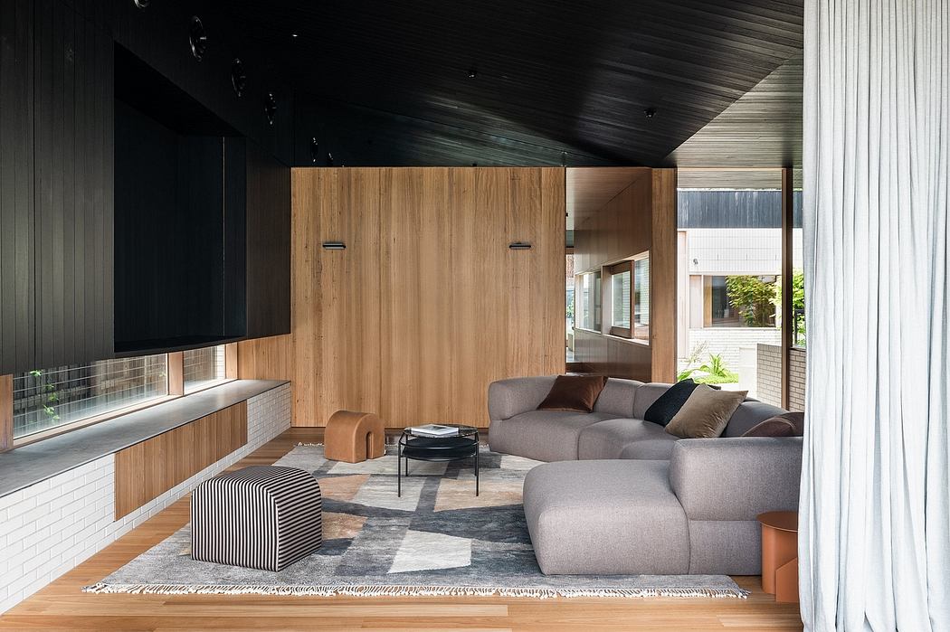 A modern living room with a dark wood-paneled wall, gray sofas, and a patterned rug.