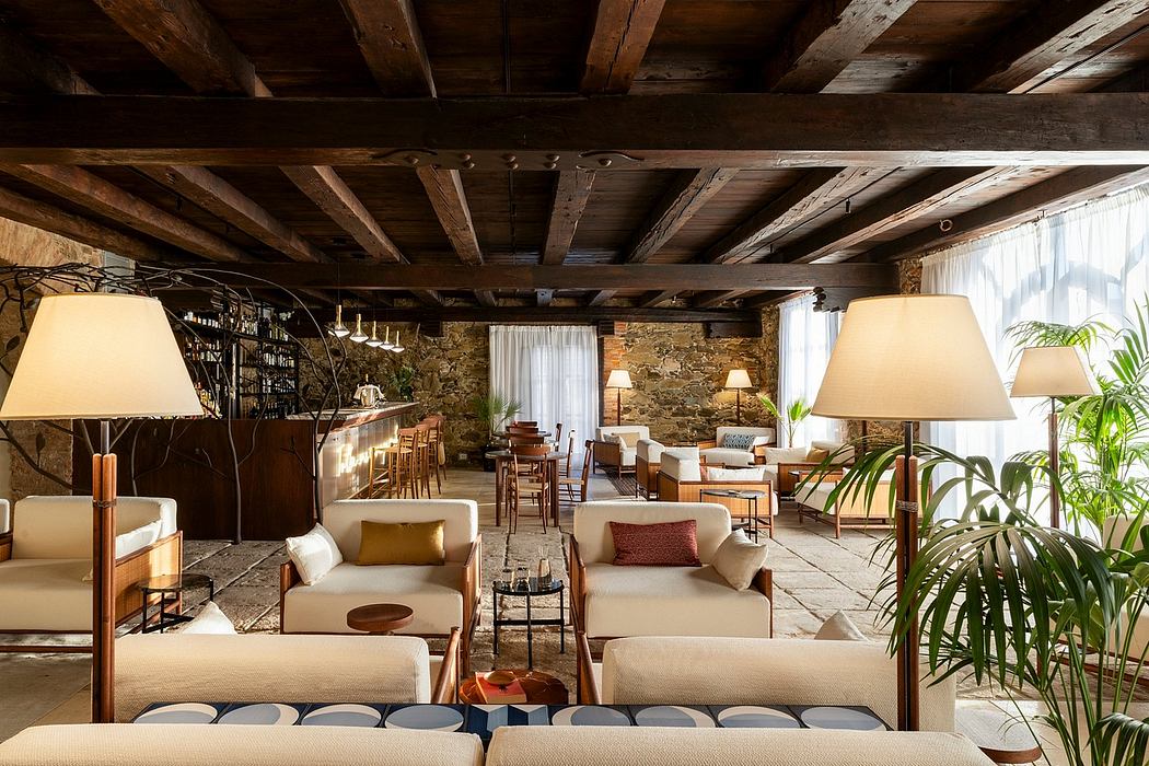 A cozy rustic lounge with exposed wooden beams, stone walls, and lush greenery.