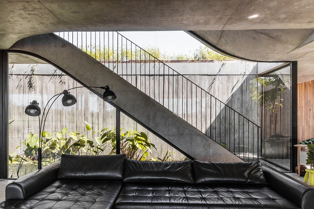 A modern, industrial-style interior with concrete walls, steel stairs, and a large black leather sofa.