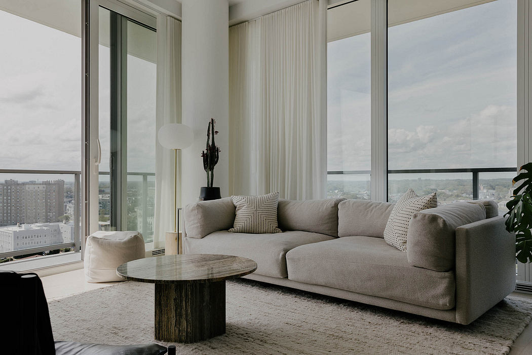 Modern living room with large windows, neutral-toned sofa, and round wooden coffee table.