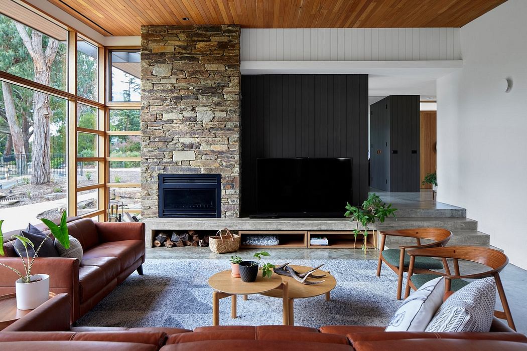 A warm, modern living room with a stone fireplace, wood-paneled ceiling, and sleek furnishings.