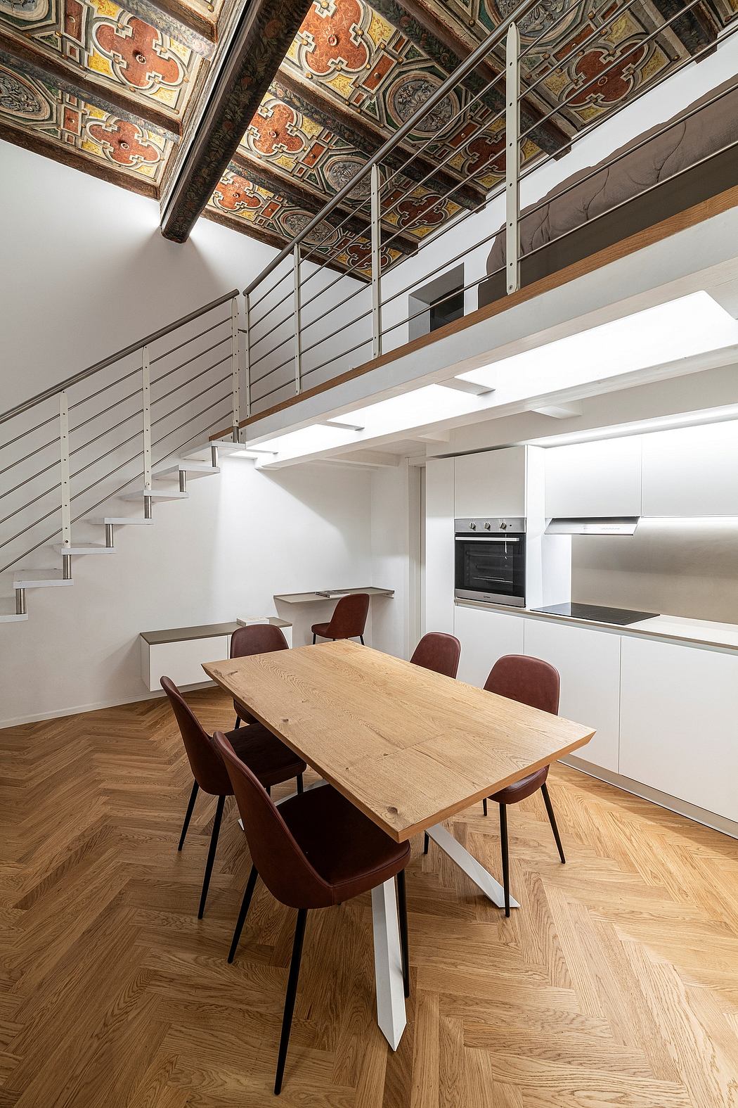 Ornate ceiling, modern kitchen, wooden dining table, and metal railing create an intriguing blend of old and new.