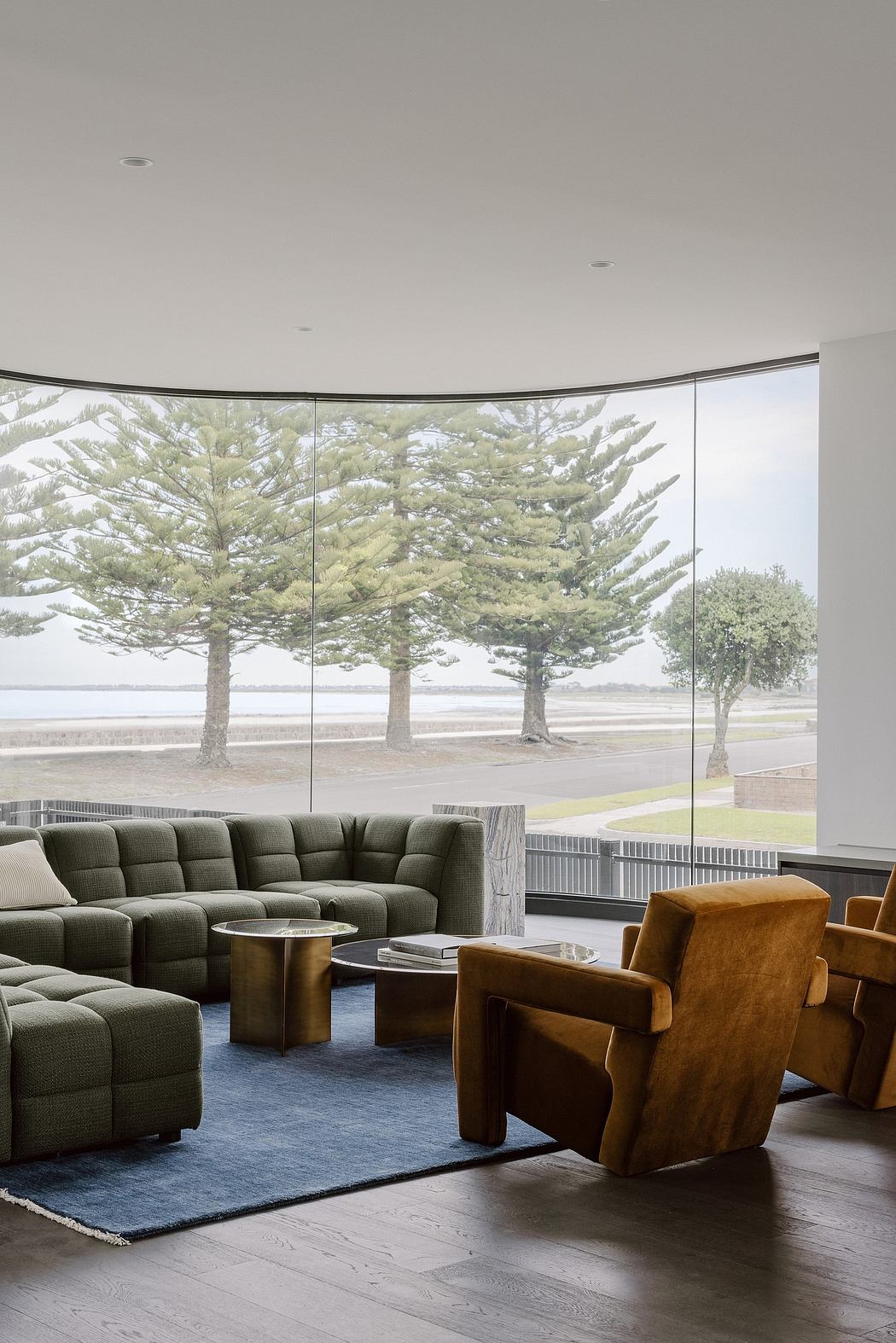 Spacious living area with large curved windows showcasing pine trees outdoors.