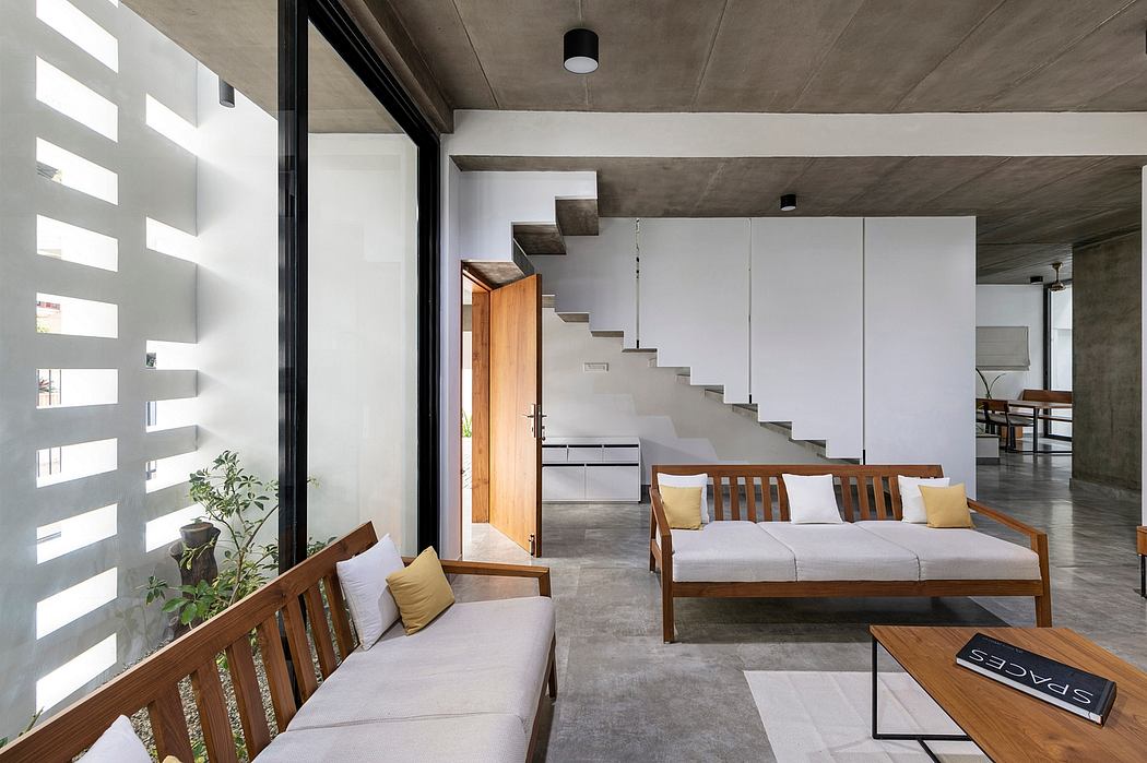 Minimalist concrete interior with wooden furniture, open staircase, and natural light.