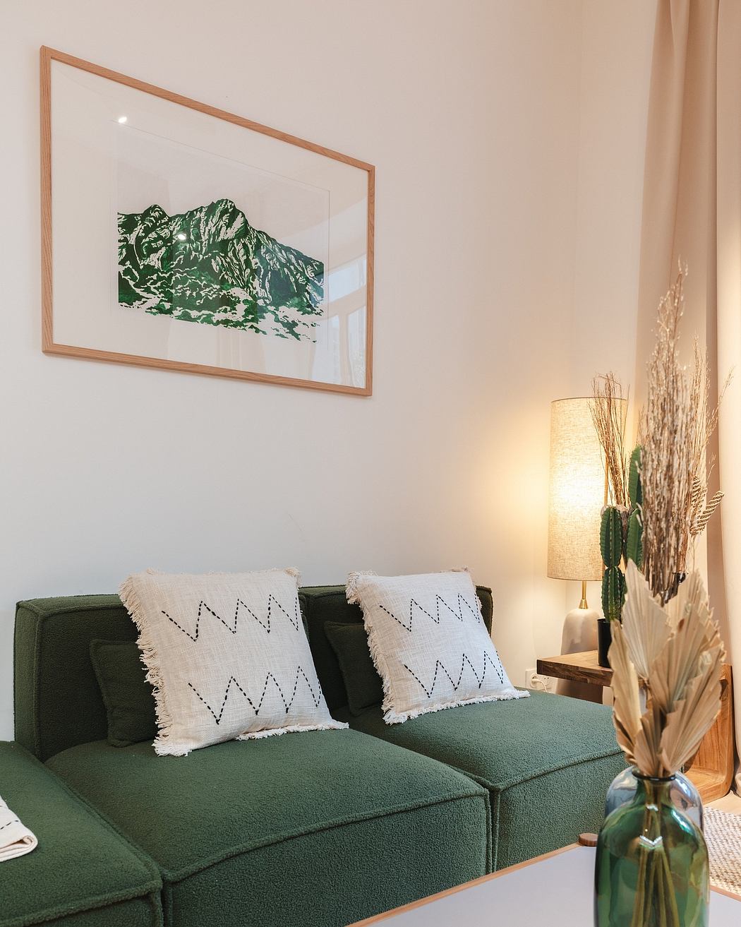 Warm, minimalist living room with framed mountain landscape artwork, textured green couch.