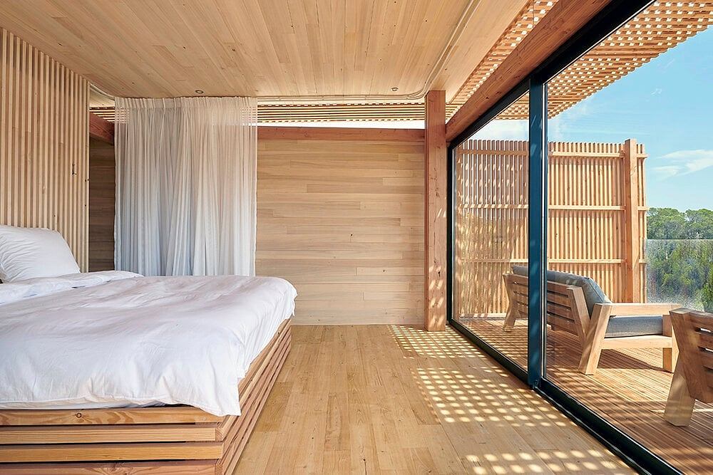 Serene wooden bedroom with minimalist design and floor-to-ceiling windows offering scenic views.