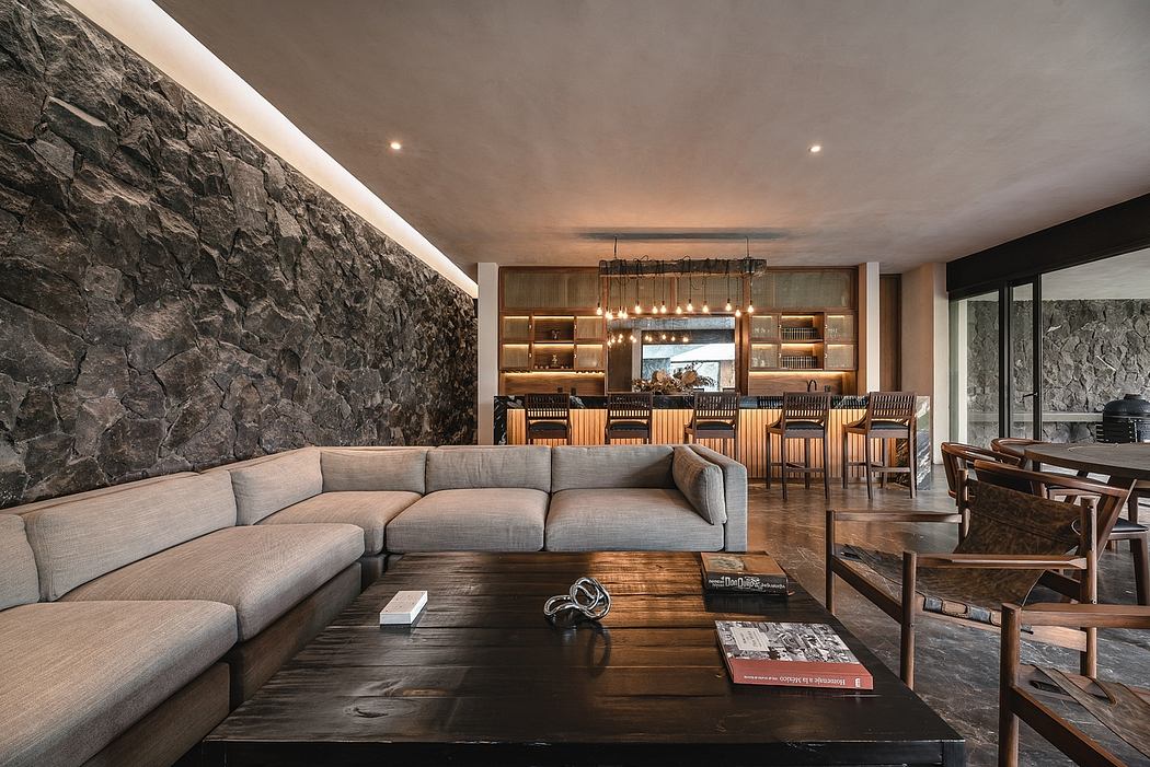 Spacious living area with stone wall, wooden furniture, and well-lit bar in background.