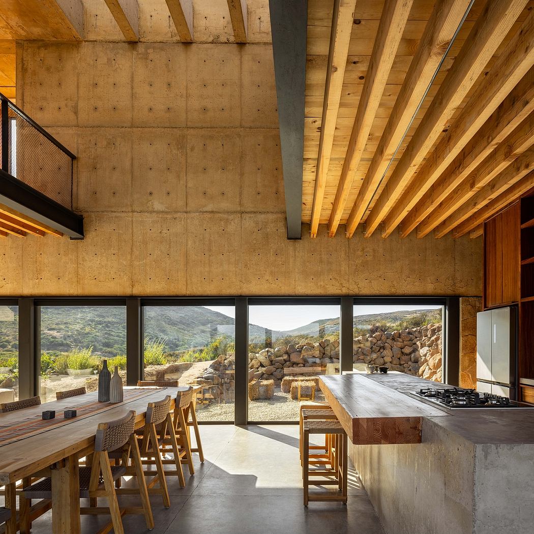 Rustic interior with exposed concrete walls, wooden beams, and floor-to-ceiling windows overlooking a mountainous landscape.