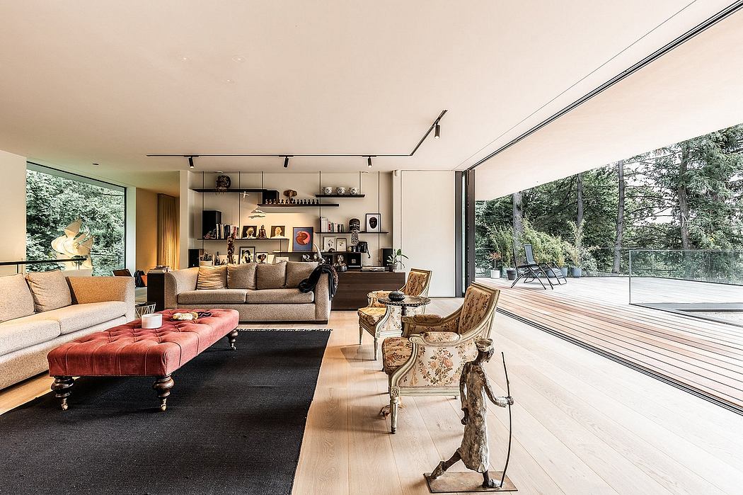 Large, open living space with a modern, minimalist design featuring plush seating, artwork, and floor-to-ceiling windows overlooking a forested outdoor area.