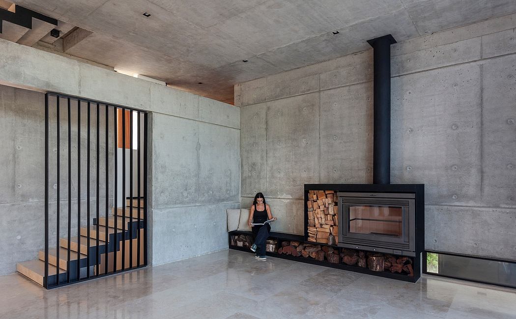 A minimalist concrete interior with a fireplace and wooden storage, featuring a person sitting on the floor.