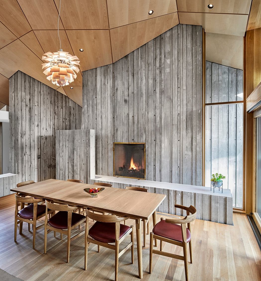 Wooden walls, modern chandelier, fireplace, and wooden dining table with chairs create a cozy, rustic ambiance.