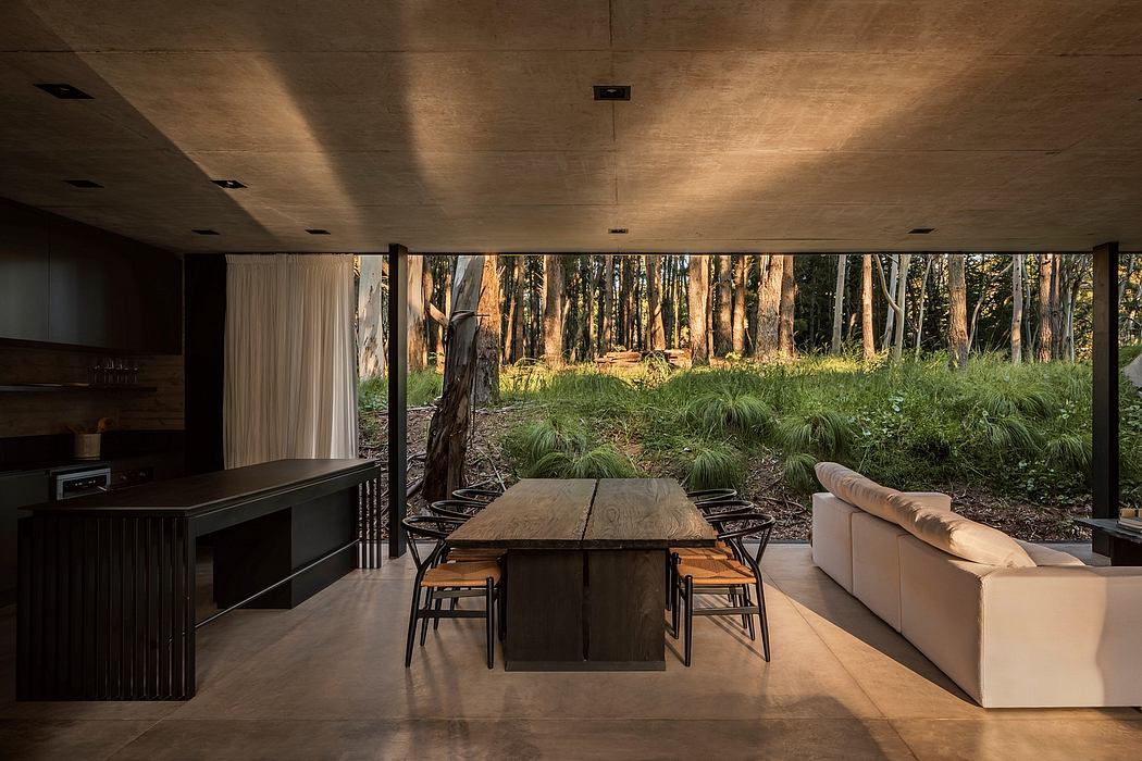 Rustic dining area with wooden table and chairs, facing floor-to-ceiling windows overlooking lush forest.