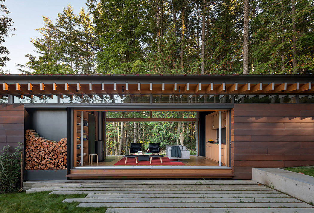 A modern, wooden cabin-style home amid lush forest trees, with a large glass wall overlooking the outdoor living space.